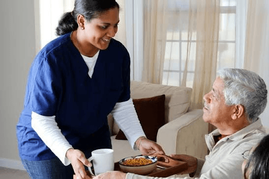 A CareBridge Lanka care coordinator serving a meal to an elderly man at home